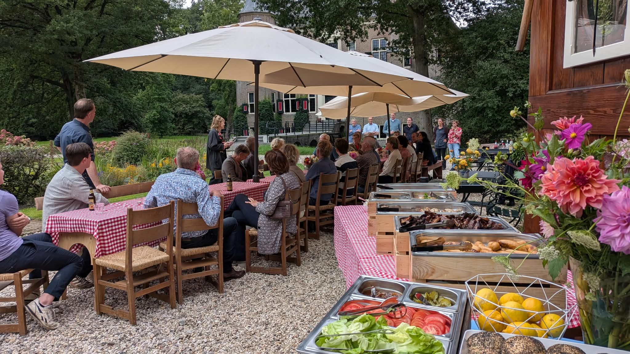 Gasten aan lange tafels bij een BBQ-catering in de tuin